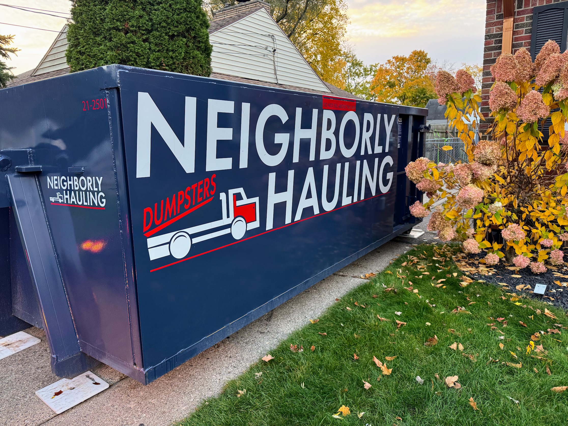 21 yard dumpster in a Grand Rapids residential driveway in fall — driveway-safe placement with Rolliskate protection boards.
