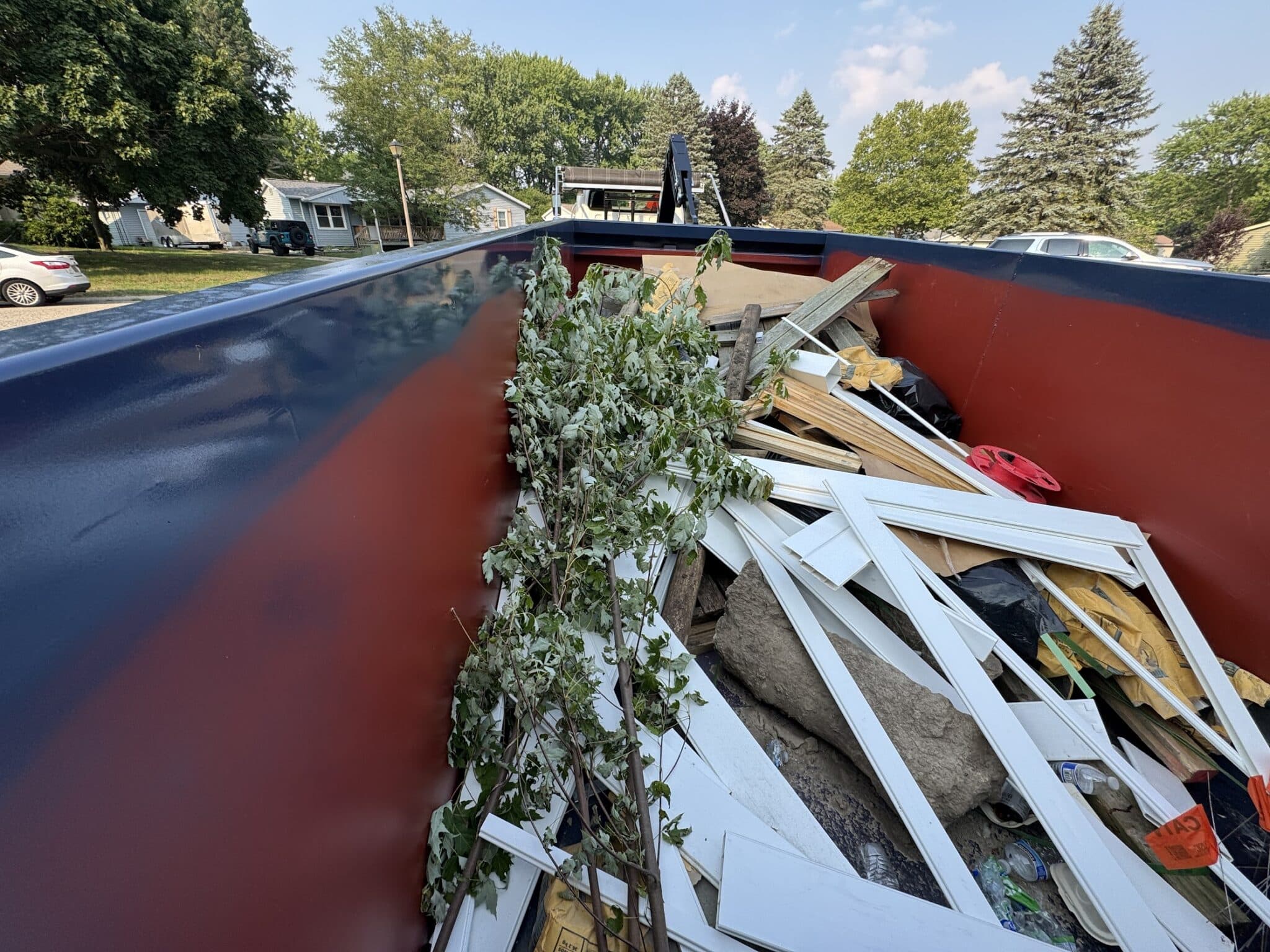 Roll-off dumpster filled with construction debris including wood trim and yard waste — properly loaded for safe transport in West Michigan.