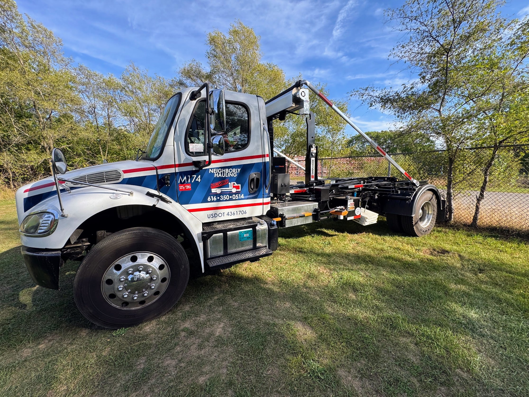 Neighborly Hauling roll-off truck delivering a dumpster in Grand Rapids, MI — licensed, insured, and CDL-certified operator.